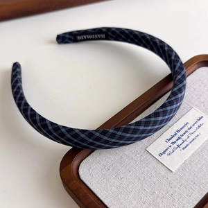Detail shot of navy plaid padded headband with handmade label inside on a wooden tray