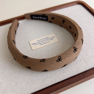 Détail du serre-tête en tissu marron avec nœuds brodés et étiquette intérieure 'HAND MADE'
