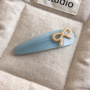 Detailed close-up of light blue acetate hair clip with a sweet cream bow and gold label