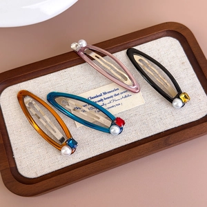 Close-up of four colorful resin BB hair clips with pearls and rhinestones on a wooden tray