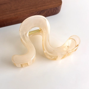 Detail shot of a semi-transparent wavy claw clip in amber cream with a gold spring