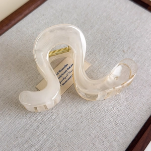 Detail of wavy irregular resin hair claw clip in beige on a textured linen background