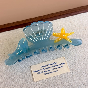 Detail of blue acetate shark hair claw clip with yellow starfish and seashell ocean motifs