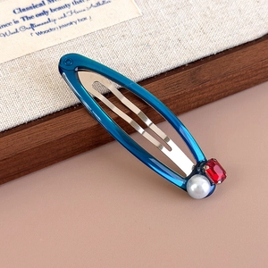 Detail of blue metal snap hair clip with red rectangular gemstone and white pearl