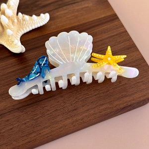 Detail of seashell hair claw with dolphins and starfish on a natural wood surface