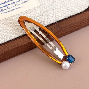 Close-up of amber resin hair clip with blue gemstone and white pearl detail