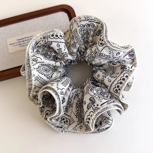 Detail shot of white scrunchie with black paisley pattern and ruffle edge