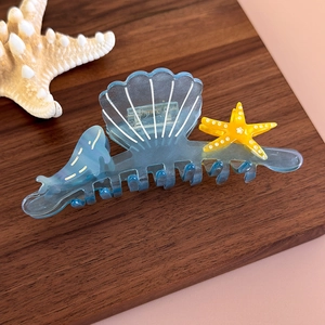 Detail of blue acetate hair claw clip featuring seashell, starfish and dolphin motifs
