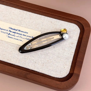 Detail of a vintage BB hair clip with yellow gemstone and pearl on dark wood tray