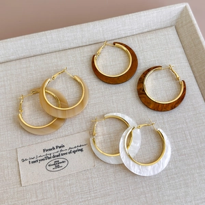 Detailed view of three pairs of C-shaped resin hoop earrings in cream and tortoiseshell