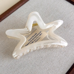 Macro shot of a cream-white star-shaped acetate hair claw clip on textured grey fabric