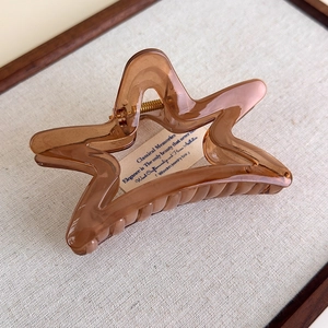 Detailed macro view of translucent brown star-shaped hair claw clip with golden spring