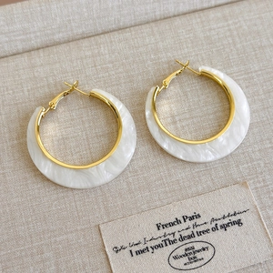 Detail of C-shaped acetate earrings with marble pattern on a beige linen background