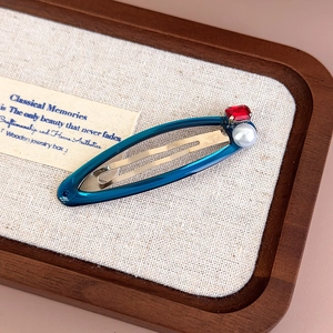 Detailed close-up of retro hair clip with blue resin, red gemstone and white pearl