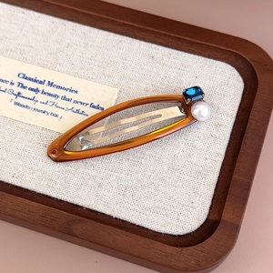 Macro detail of amber resin hair clip with blue gemstone and white pearl inlay