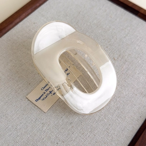 Close-up of a cream-colored hollow oval hair claw clip on a minimalist linen background