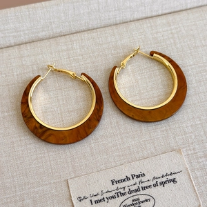 Detailed close-up of C-shaped earrings with gold metal inner and brown acetate outer ring