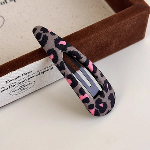 Detail of tear-drop leopard print hair clip with pink accents on a velvet jewelry tray