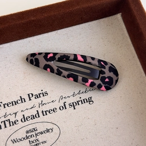 Detail of leopard print BB hair clip with pink accents on rustic linen display tray