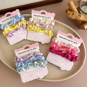 Three-piece set of satin scrunchies in various vibrant colors on a ceramic tray