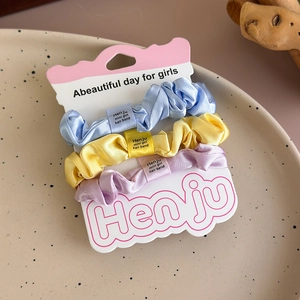 Detailed view of satin scrunchies in blue, yellow, and purple on branded display card