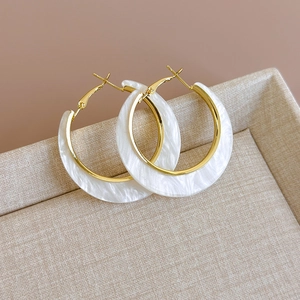 Detail view of C-shape gold and white resin earrings on a beige linen display box