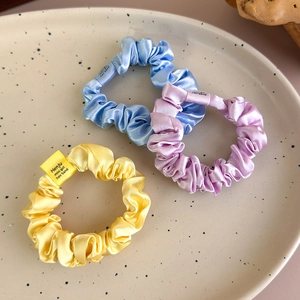 Close-up of three colorful satin scrunchies in blue, purple, and yellow on a tray