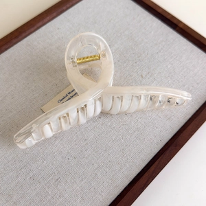 Detail of a large cream-colored hair claw clip with a twisted loop design on a linen board