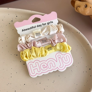 Close-up of three satin scrunchies in cream, pink, and yellow on a ceramic tray