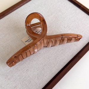 Macro detail of amber acrylic hair claw clip with metal spring on fabric display