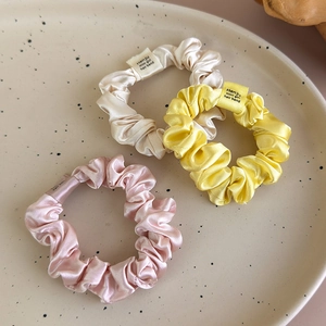 Close-up of three satin scrunchies in cream, yellow, and pink colors on a ceramic tray