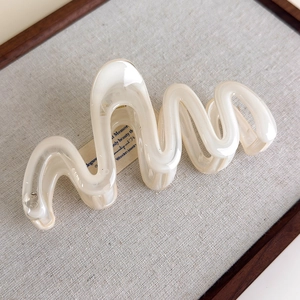 Close-up of wavy cream hair claw clip on a linen texture tray in a soft aesthetic setting