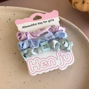 Three satin scrunchies in lavender, blue and mint green on a white display card