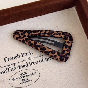 Macro detail of leopard print fabric BB hair clip with textured metal base on soft canvas