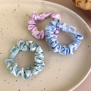 Close-up of three satin hair scrunchies in lilac, sky blue and green on a ceramic plate