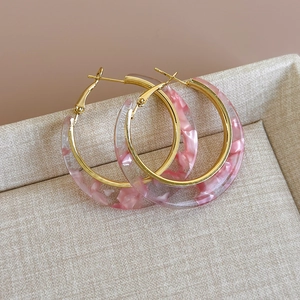 Detail view of large C-shaped hoop earrings with pink marble acetate and gold metal frames