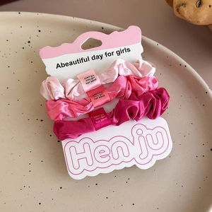 Detailed view of 3-pack pink satin scrunchies set on minimalist cardboard packaging