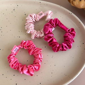 Close-up of three satin scrunchies in pink and purple shades on a ceramic tray