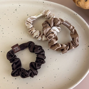 Detailed view of three satin scrunchies in champagne and bronze tones with woven tags