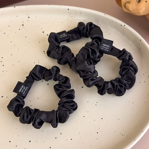 Close-up of three black satin scrunchies with smooth texture and woven labels on a tray