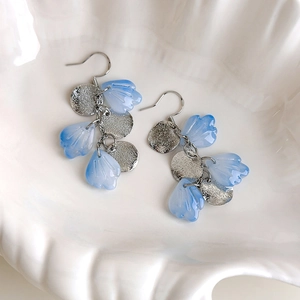 Macro shot of gradient blue petal earrings with silver textured discs on shell tray