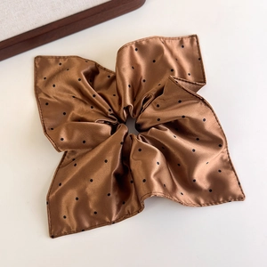 Close-up of brown polka dot satin scrunchie with soft silk-like texture and folds
