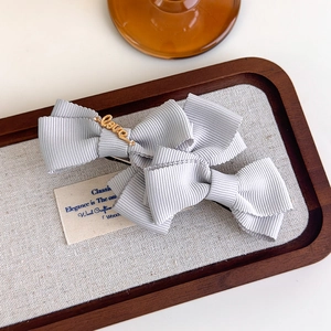 Close-up of light grey bow hair clip with gold Love metal lettering and ribbed texture