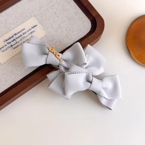 Detail of grey bow hair clip with gold Love charm on a wooden tray with linen background