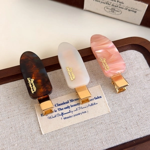 Detailed macro of tortoiseshell acetate hair clips with golden brand accents on wood