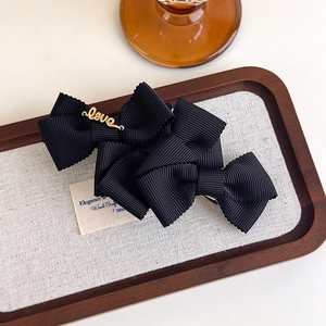 Detail of black bow hair clips with Love metal accent on a textured wooden tray