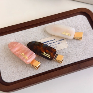 Detailed view of three colorful acetate hair clips with gold metal logo on linen tray