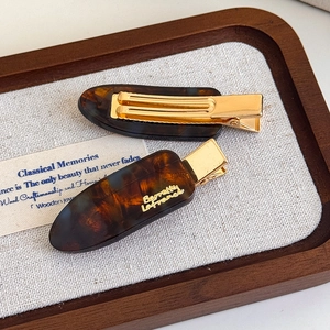 Close-up of tortoiseshell acetate hair clips with gold metal base and artistic branding