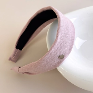Detail of light pink knitted headband featuring a silver heart charm on white ceramic