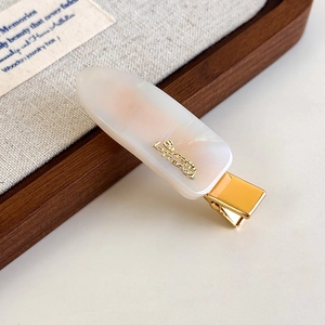 Detailed close-up of a pearly white marble acetate hair clip with a golden metal logo